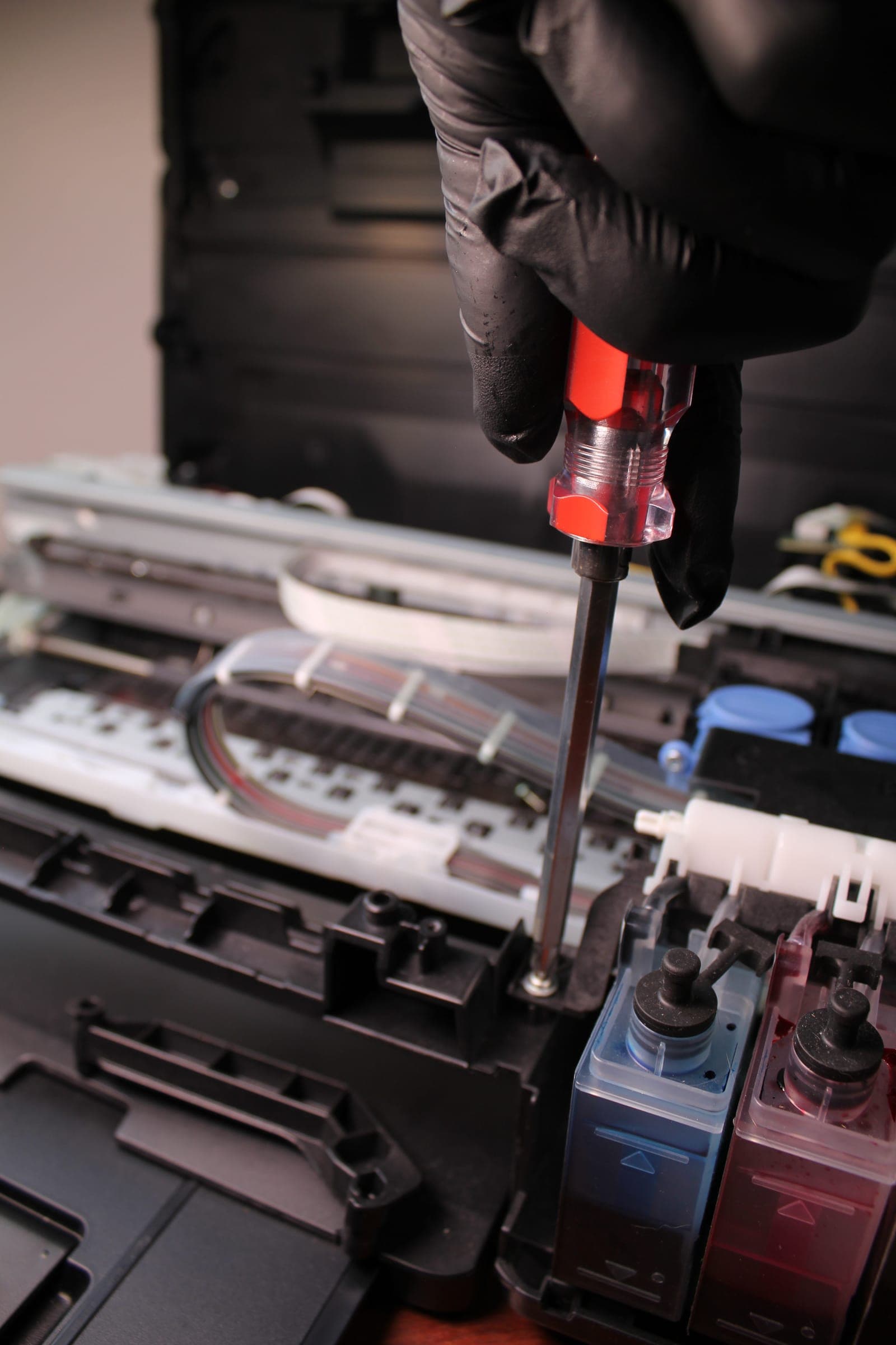Técnico con guantes ajusta con un destornillador el sistema de tanques de tinta de una impresora abierta.